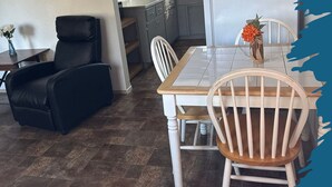 A dining area with a white table and chairs, a black leather chair, and a vase with flowers. - 11 - 1 king, 1 full, 1 queen, 2br, 1ba suite (Challenge-Brownsville)