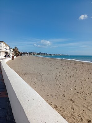 Uma extensa praia de areia com uma parede branca de um lado e um céu azul e límpido.
