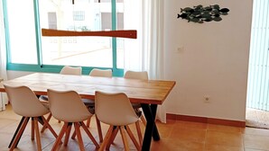 Een eethoek met een houten tafel en vier stoelen, grote ramen met uitzicht op gebouwen, en een visdecoratie aan de muur.