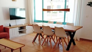Een woonkamer met een televisie, een eettafel met stoelen, een bank en een plafondventilator.
