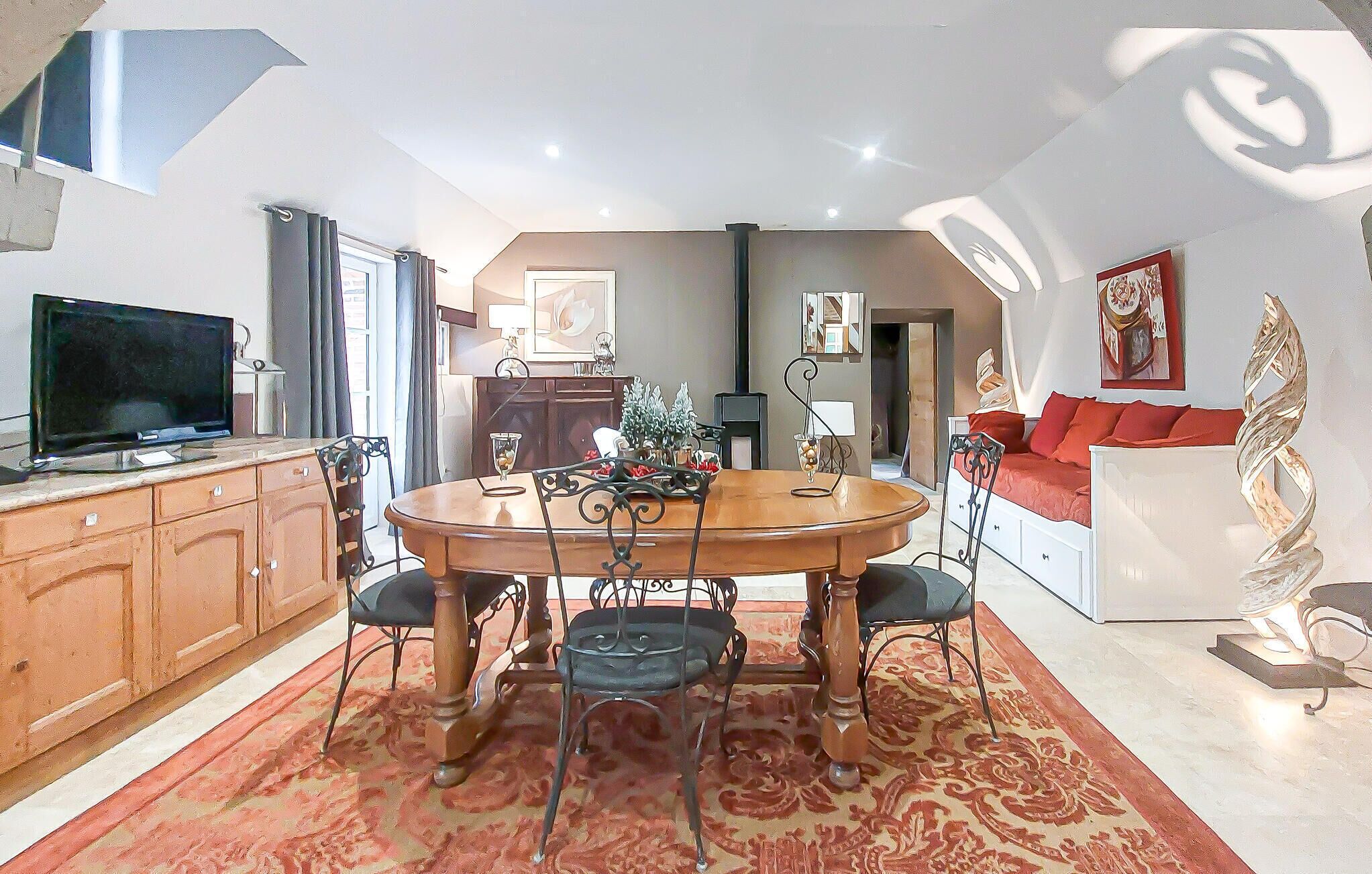 A dining area with a round table, chairs, and a TV on a cabinet.