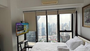 A hotel room with a bed, a TV, a window with a city view, and a framed picture on the wall. - STAYLUXIA Knightsbridge Delux 1BR, FREE Amenities, Pool, Netflix, Panoramic View (Makati)