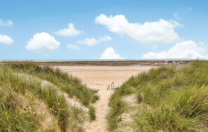 Un sentier qui longe la plage et mène à une étendue de sable, avec des dunes de chaque côté.