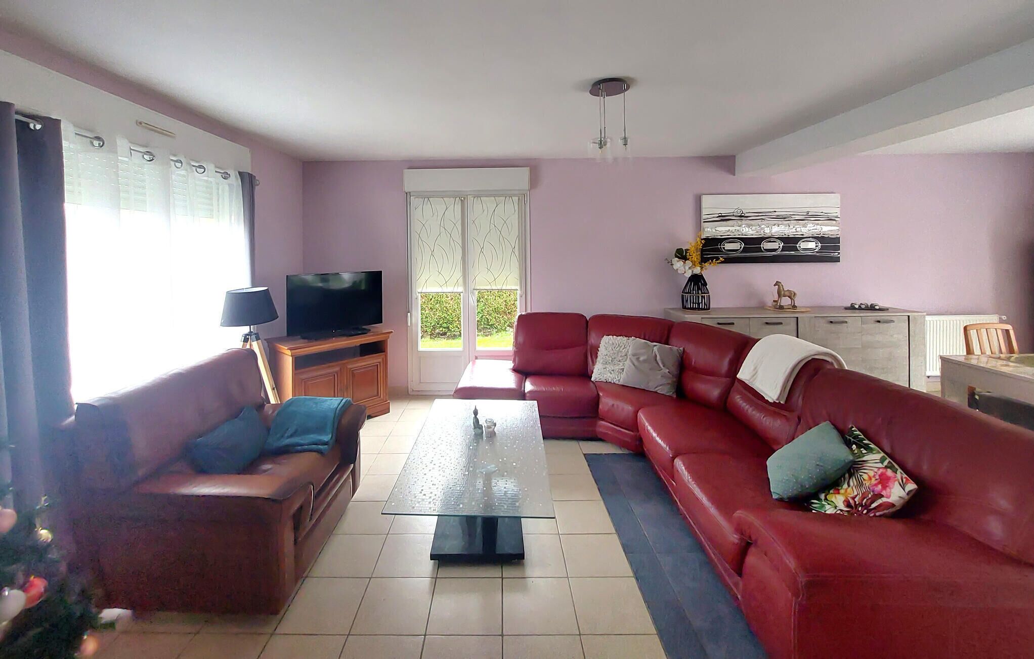 Un soggiorno con un divano rosso, una televisione su un mobile in legno e una finestra con tende.