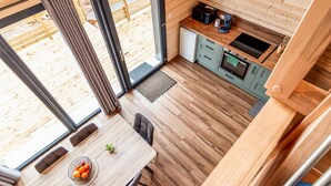 Une cuisine de taille réduite avec un intérieur en bois, un coin repas comprenant une table et des chaises, et une vue sur l’extérieur grâce à de grandes fenêtres.