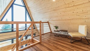 Un loft moderne avec un intérieur en bois, un escalier en bois, une vue dégagée grâce à de grandes fenêtres et un petit coin salon avec une chaise et une table.
