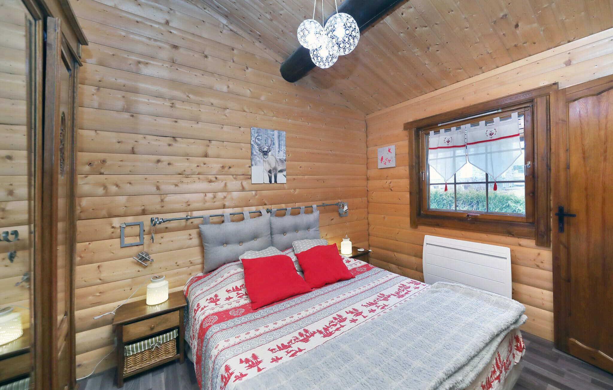 Ein gemütliches Schlafzimmer in einer Holzhütte, mit einem Bett, einem Fenster mit Vorhängen, einem Wandbild und einer Deckenleuchte.