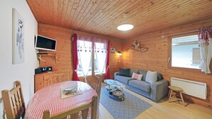 A cozy cabin interior with a wooden ceiling, a dining table with a checkered tablecloth, a sofa, a rocking chair, and a television. - Amazing apartment in Gerardmer with lake view (Gerardmer)