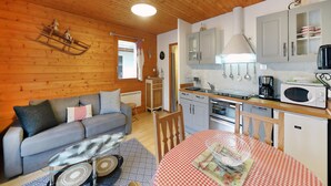 A cozy cabin-style room with a sofa, a dining table with a checkered tablecloth, a kitchen with a microwave, and a hanging light fixture. - Amazing apartment in Gerardmer with lake view (Gerardmer)