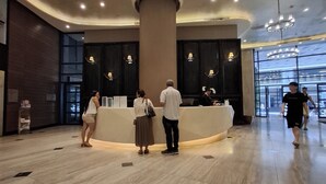 A hotel reception area with a curved reception desk, a large pillar, and a glass entrance. - STAYLUXIA Knightsbridge Luxury 1BR with Balcony, FREE Pool, Netflix, Cityview (Makati)