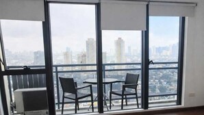 A hotel room with a large window, a bed, and a balcony with chairs. - STAYLUXIA Knightsbridge Luxury 1BR with Balcony, FREE Pool, Netflix, Cityview (Makati)