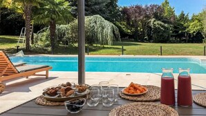 Desayuno junto a la piscina con aperitivos, bebidas y vistas a una piscina y zonas verdes.