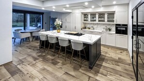 Una cocina moderna con una isla de mármol, taburetes de bar y un amplio ventanal con vistas a un jardín.