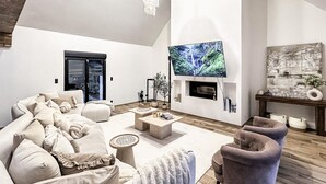Una sala de estar moderna con un televisor de pantalla plana grande montado en la pared, una chimenea y una zona de estar acogedora con un sofá y sillones.