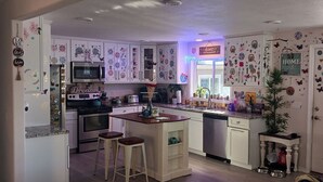 Una cucina con mobili bianchi, un'isola centrale con sgabelli, un forno a microonde, un fornello e una lavastoviglie.