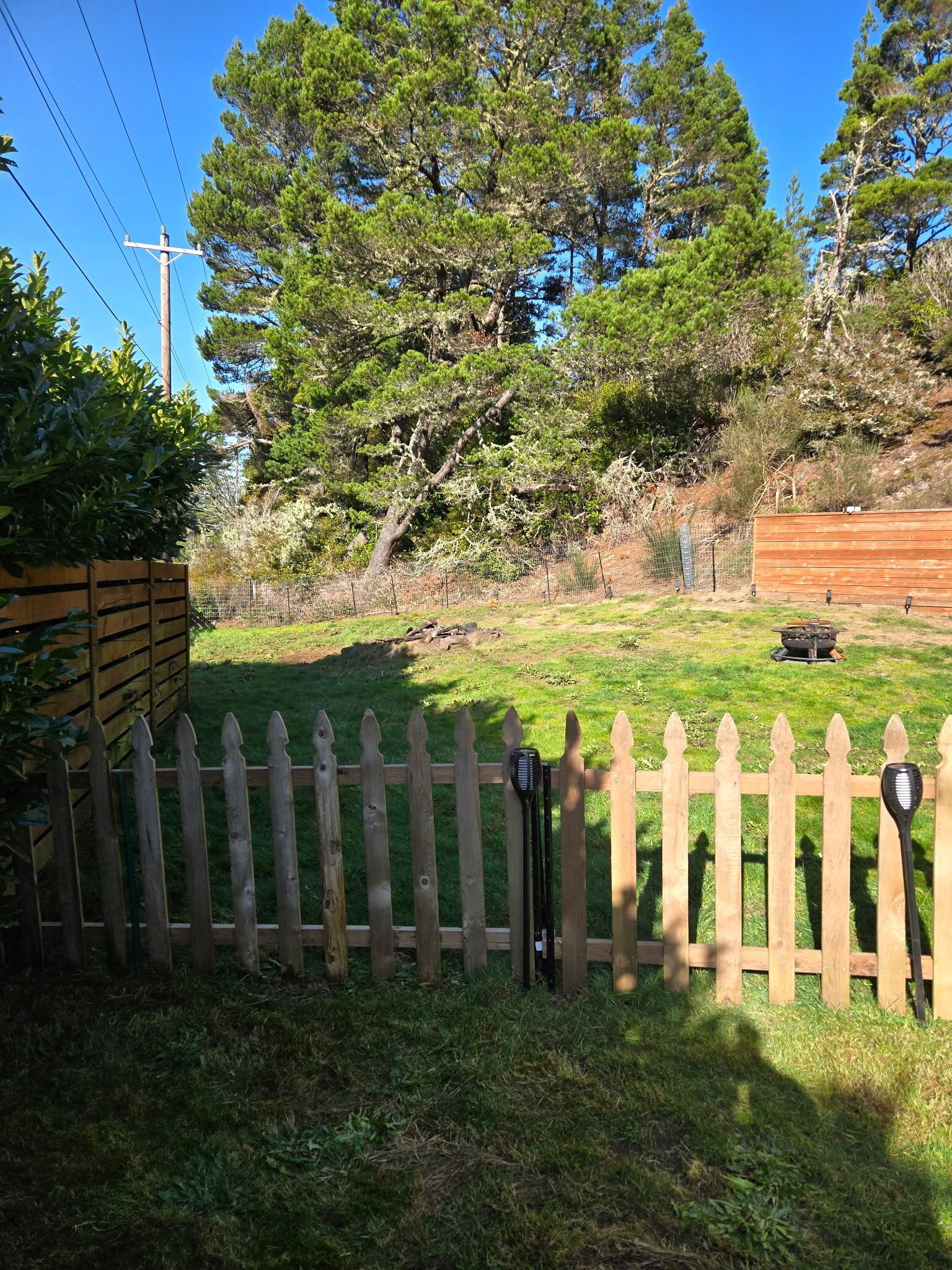 Une cour arrière clôturée, avec une clôture en bois, un barbecue et un abri de jardin en bois.
