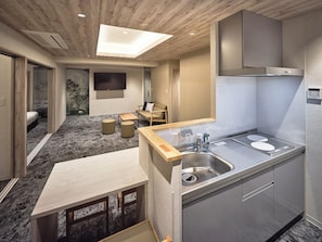 Ein modernes Hotelzimmer mit Holzboden, einem Flachbildfernseher, einem Sofa, einem Couchtisch, einem Waschbecken und einer eingebauten Schrankwand.