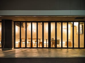 A restaurant with a modern interior, featuring wooden tables and chairs, and a view through large glass doors. - WELLSTAY Namba Apartmenthotel-Cocochill (Osaka)