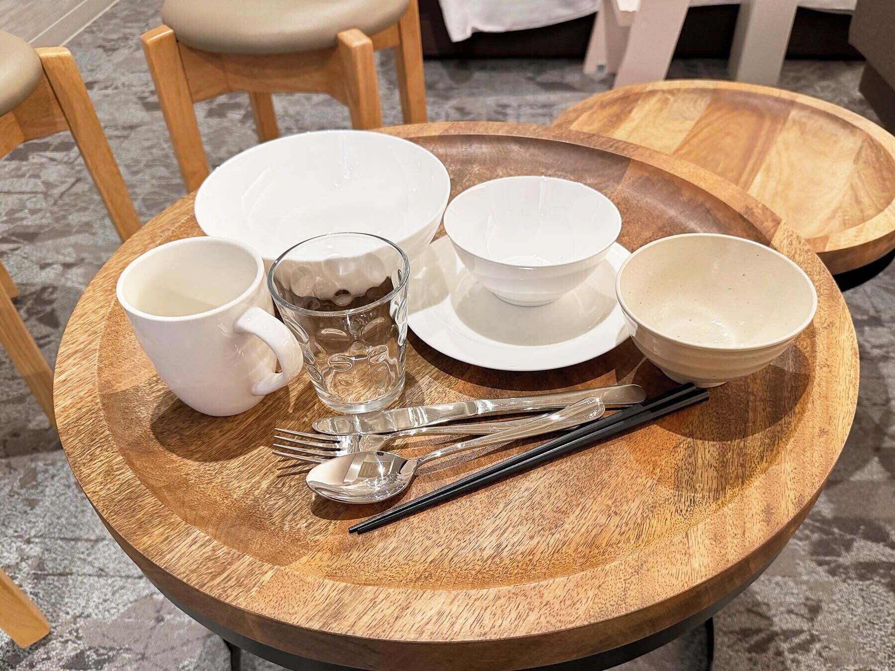 Een ronde houten tafel met een dienblad waarop witte kommen, een glazen mok en bestek staan.