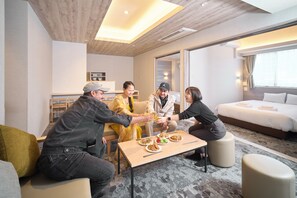 A group of people seated around a table with food, in a room with a bed and a window. - WELLSTAY Namba Apartmenthotel-Cocochill (Osaka)