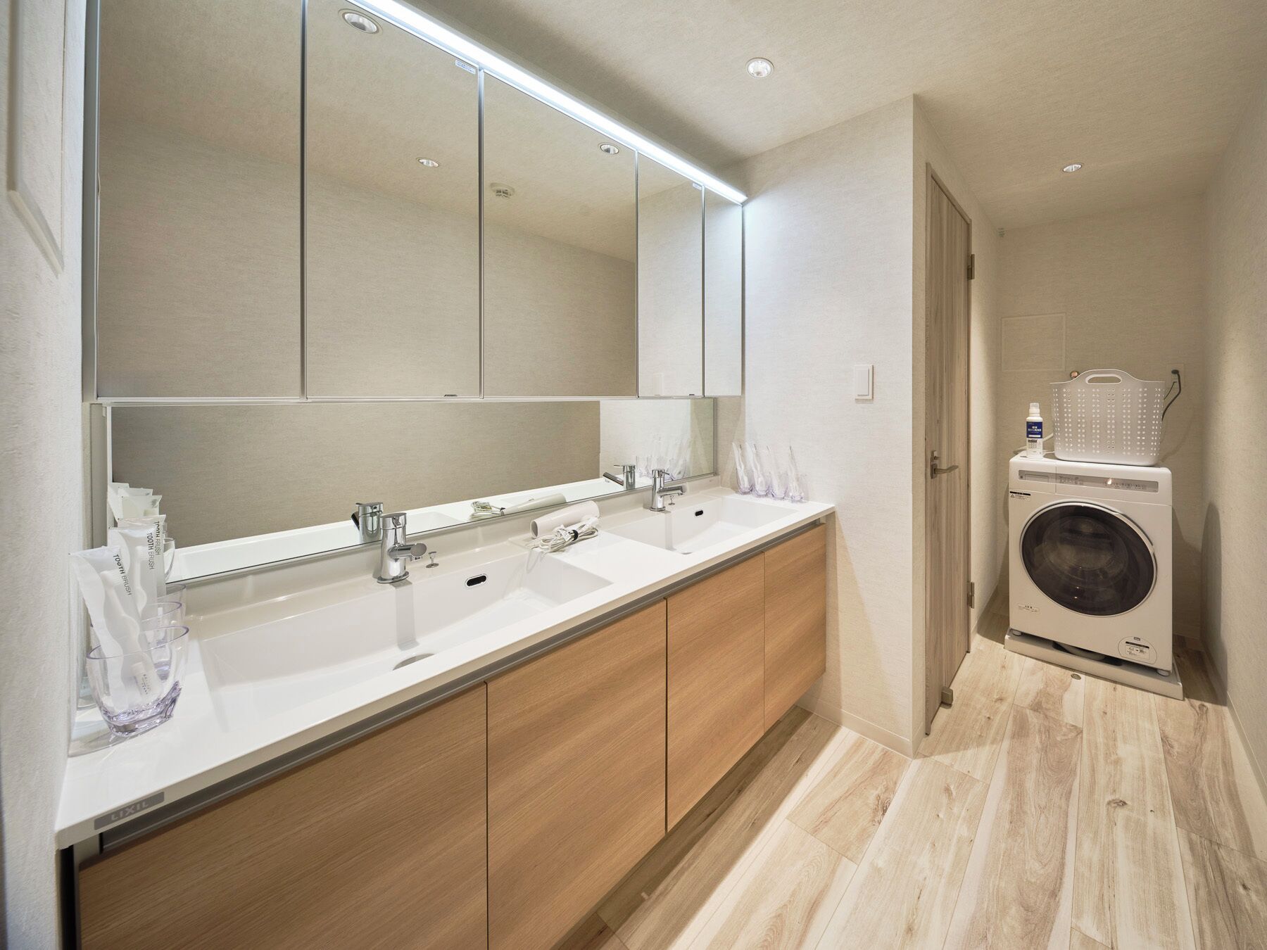Een moderne badkamer met een dubbele wastafel, een grote spiegel en een ingebouwde wasmachine.