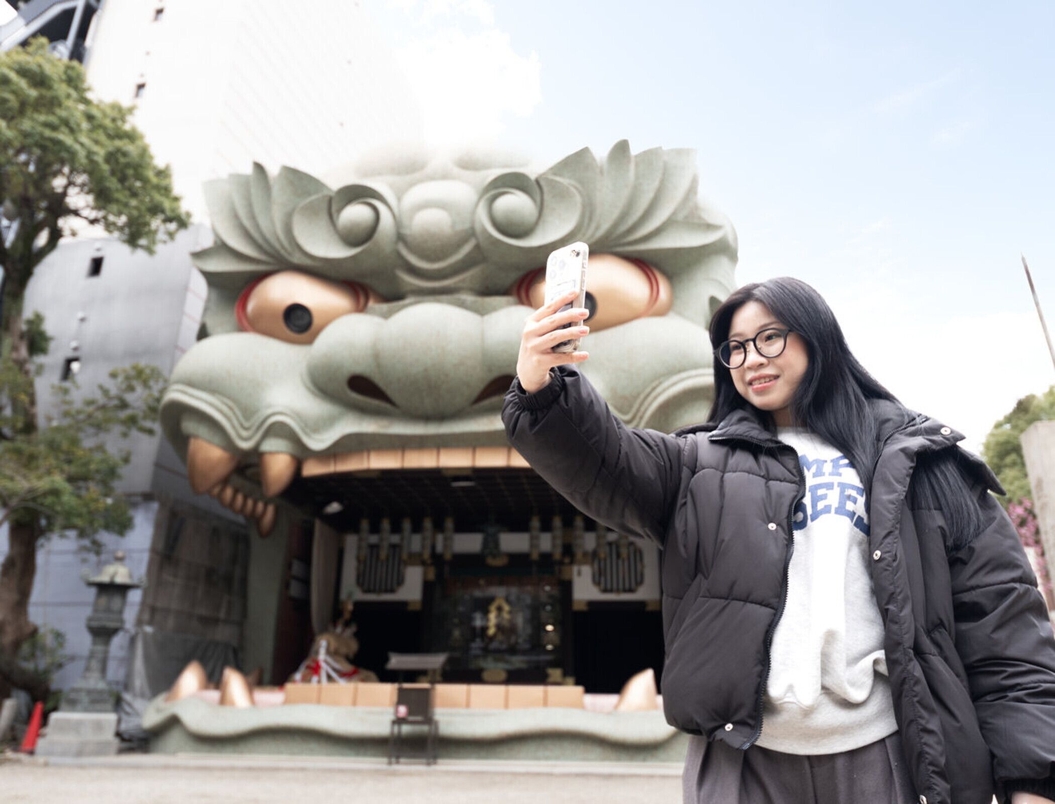 A person taking a selfie with a large, stylized animal head sculpture in the background.