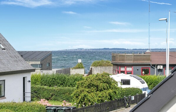 A coastal view with a white RV parked in front of a building with a red door, surrounded by greenery and a clear sky.
