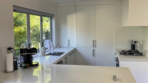 Uma cozinha moderna com armários brancos, uma ilha central com banquetas, fogão embutido e uma janela que oferece iluminação natural.