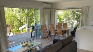 Uma sala de estar moderna com um sofá grande, uma mesa de centro de vidro e uma área de jantar com cadeiras de vime.