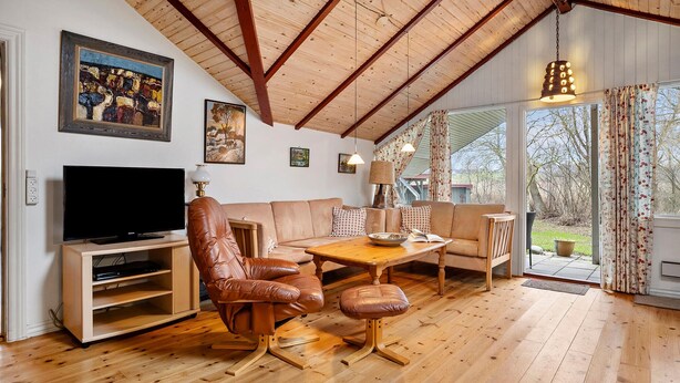 Ein gemütliches Wohnzimmer mit Holzboden, einem Ledersessel, einer Couch, einem Couchtisch und einem Fernseher auf einem Holzboden.