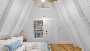 Un dormitorio con techo inclinado, una cama con ropa de cama blanca, un ventanal con vistas y una puerta.