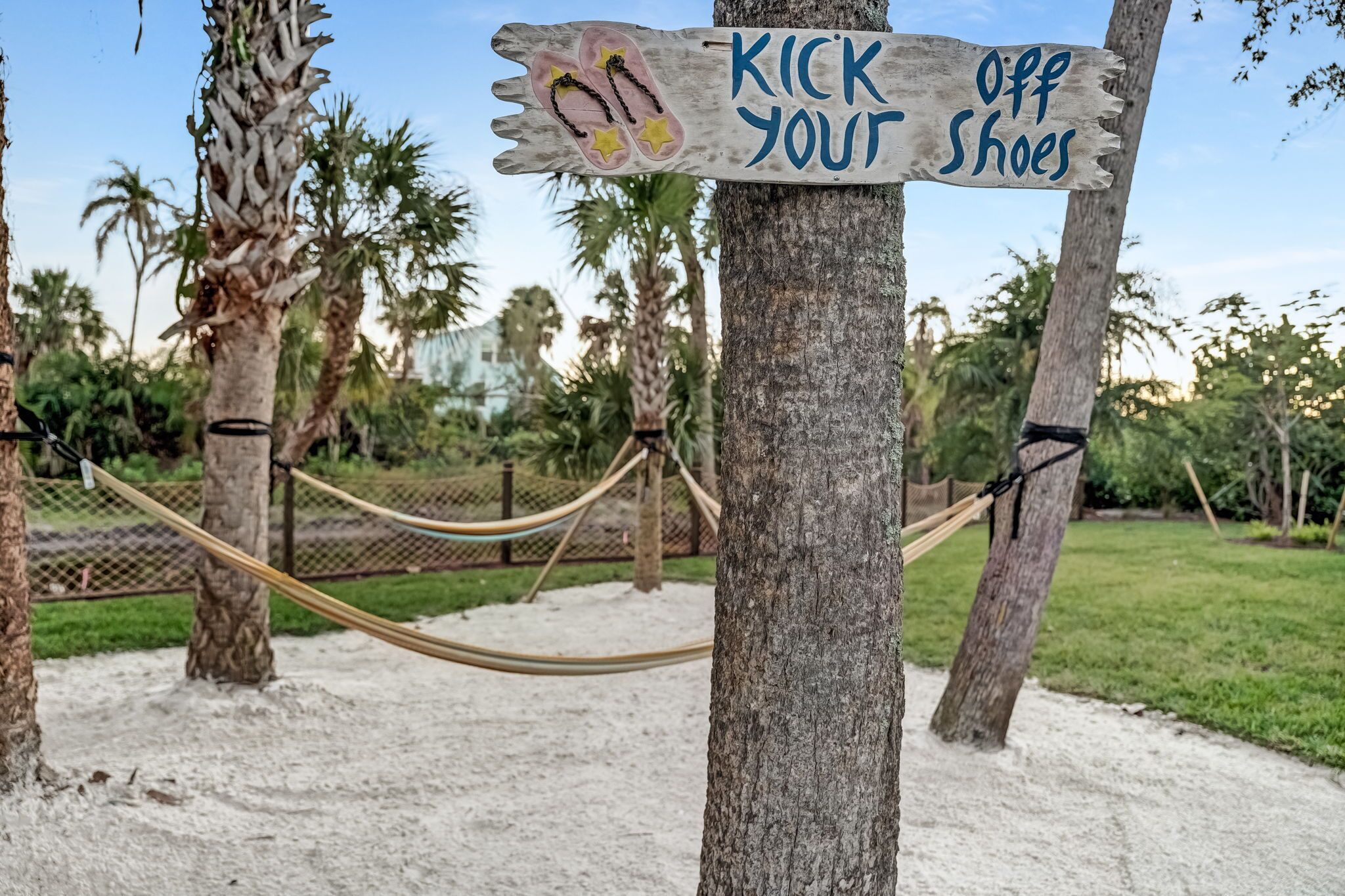A sign on a tree that reads "KICK OFF YOUR SHOES" with a pair of flip-flops and stars.