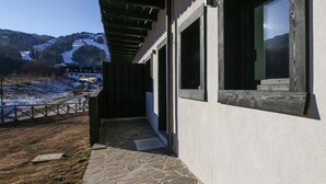 A modern building with large windows, a stone-paved entrance, and a view of a snowy landscape and mountains in the background.