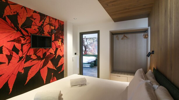 A hotel room with a bed, a wall-mounted TV, a door leading outside, and a view of a car parked outside.