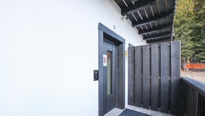A wooden door with a no smoking sign, a small outdoor area with a stone floor, and a wooden fence.