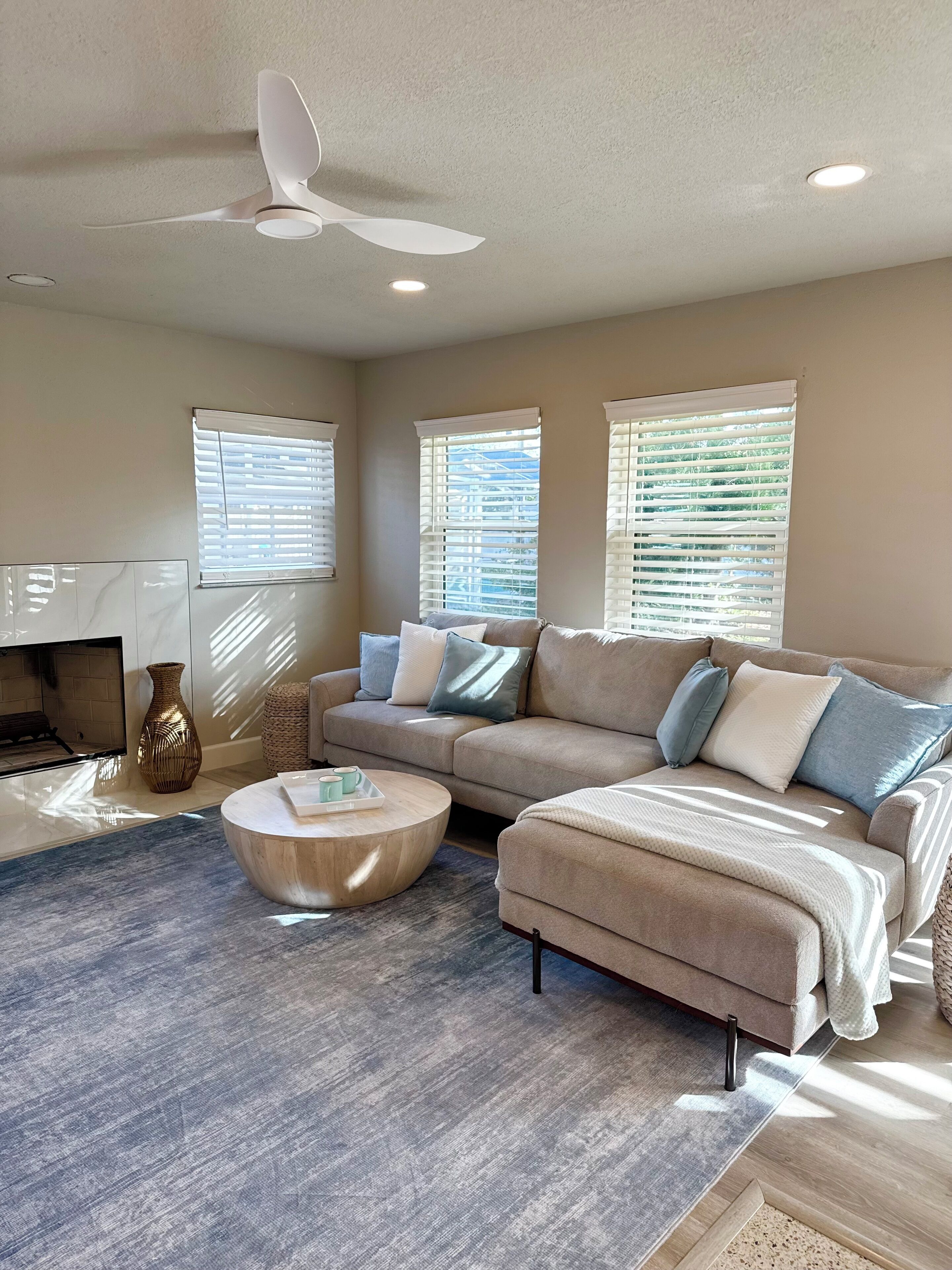 A modern living room with a beige sofa, a round coffee table, and a ceiling fan.