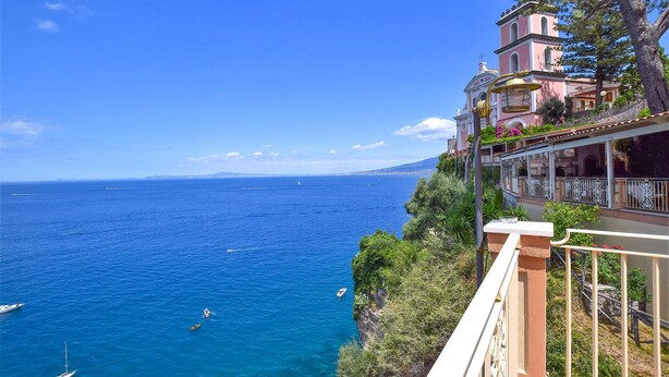 Paesaggio costiero con un edificio rosa, caratterizzato da balconi e un campanile.