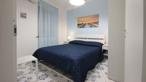 Una camera da letto con un letto, un comodino, una lampada, un quadro appeso al muro e una finestra con tende.
