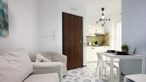 Un soggiorno con divano e tavolo da pranzo con sedie, una cucina sullo sfondo e un pavimento decorato.
