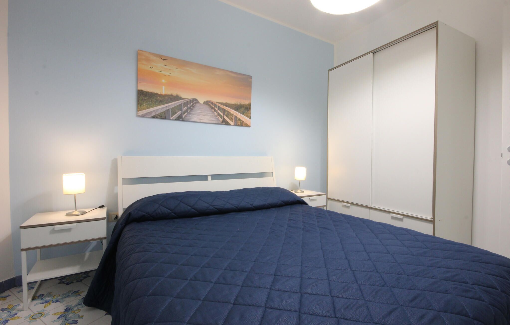 Une chambre à coucher avec un lit, des tables de chevet, un tableau et une armoire.