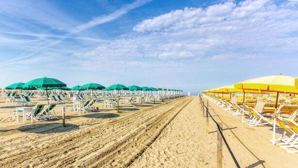Ein Strand mit Liegestühlen in Reihen unter grünen und gelben Sonnenschirmen, die in abwechselnden Mustern angeordnet sind.