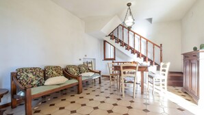 Ein Wohnzimmer mit einer Sofagarnitur, einem Esstisch mit Stühlen, einer Treppe und einem Schrank.