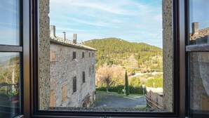A rustic stone building with multiple windows and a view of a forested hillside. - Cozy apartment in Montecastelli Pisano (Montecastelli Pisano)