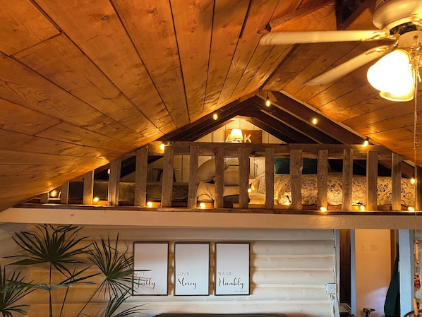 An attic bedroom with wooden beams, a sloped ceiling, and a bed with patterned bedding.