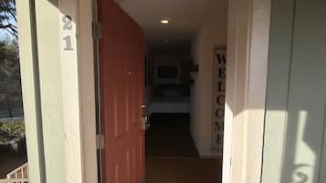 A hallway with a red door, a welcome sign, and a bed in the background.