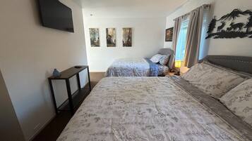 A bedroom with two beds, a TV mounted on the wall, and three paintings on the wall.