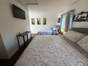 Une chambre avec deux lits, un téléviseur fixé au mur et trois tableaux accrochés au mur.