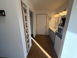 Un pasillo estrecho con un cartel de bienvenida, una puerta, un lavamanos y un espejo.