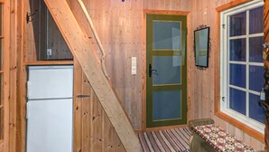 Eine kleine Holzhütte mit Holzinnenraum, einer Tür, einem Fenster, einer Bank und einem Kühlschrank.