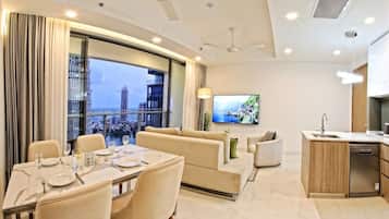 A modern living room with a dining area, a sofa set, a television, and a kitchen area with a dishwasher.